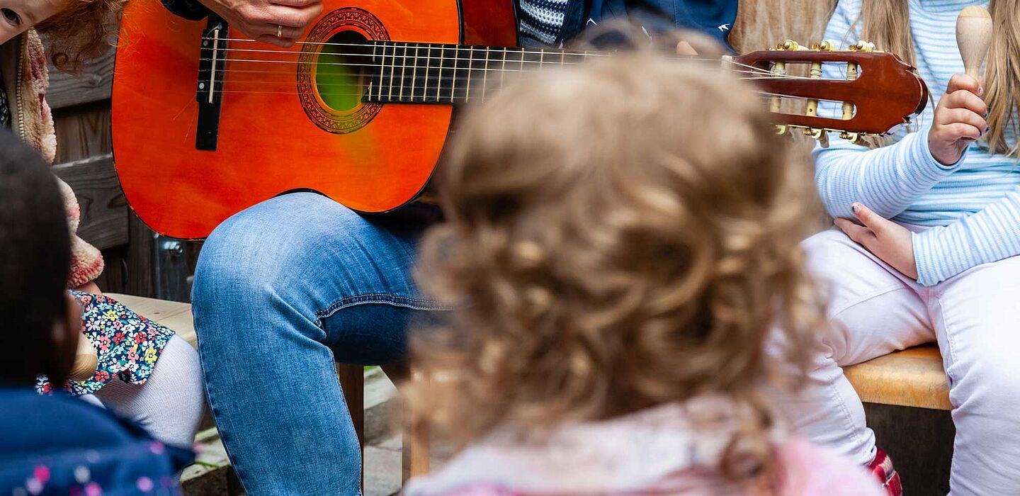 Kinder hören einem Erzieher zu, der Gitarre spielt